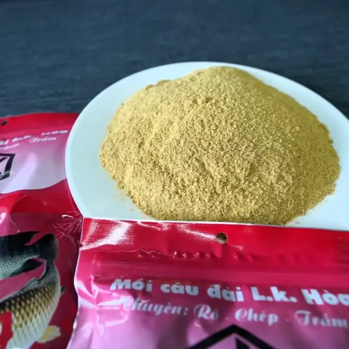 Mồi Câu Đài LK dạng cốt cám mịn có độ đạm cao được đổ ra đĩa trắng bên cạnh bao bì